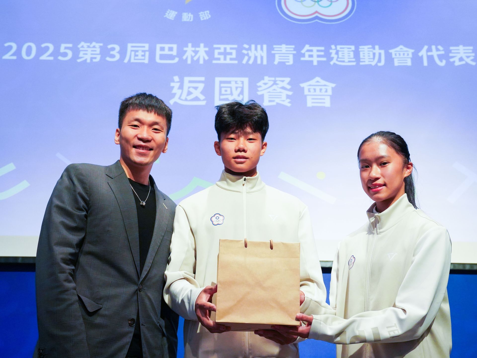 運動部長李洋致贈禮品，由黃迺軒（中）、潘筱晴（右）選手代表接領。（運動部提供）