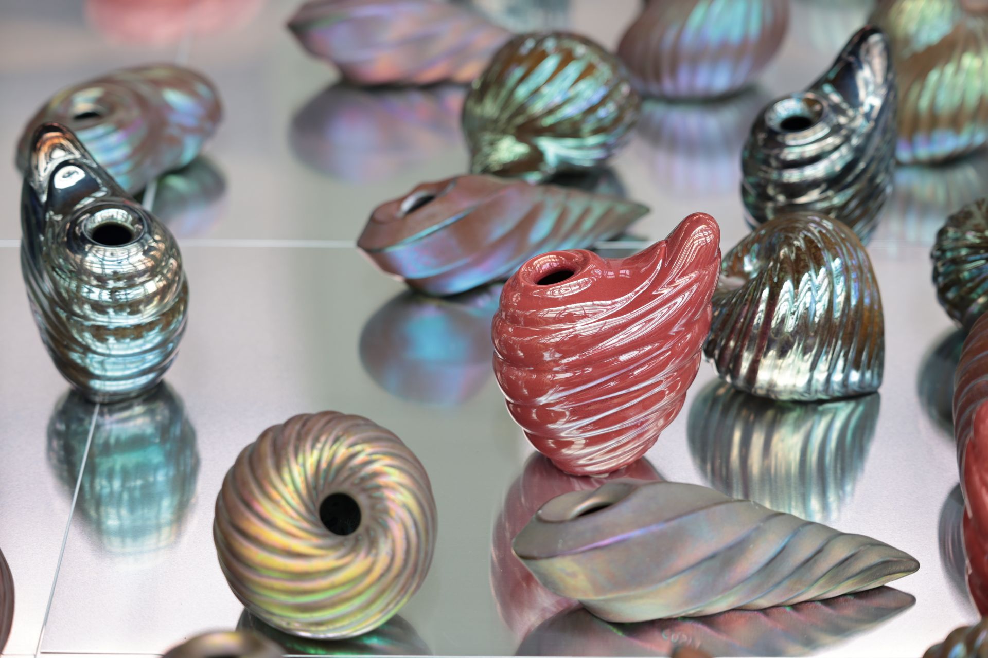 數百件螺旋或水滴狀陶製貝殼覆以粉紅、藍綠、紫色金屬光澤，隨光線閃爍變幻。（鶯歌陶博館提供）