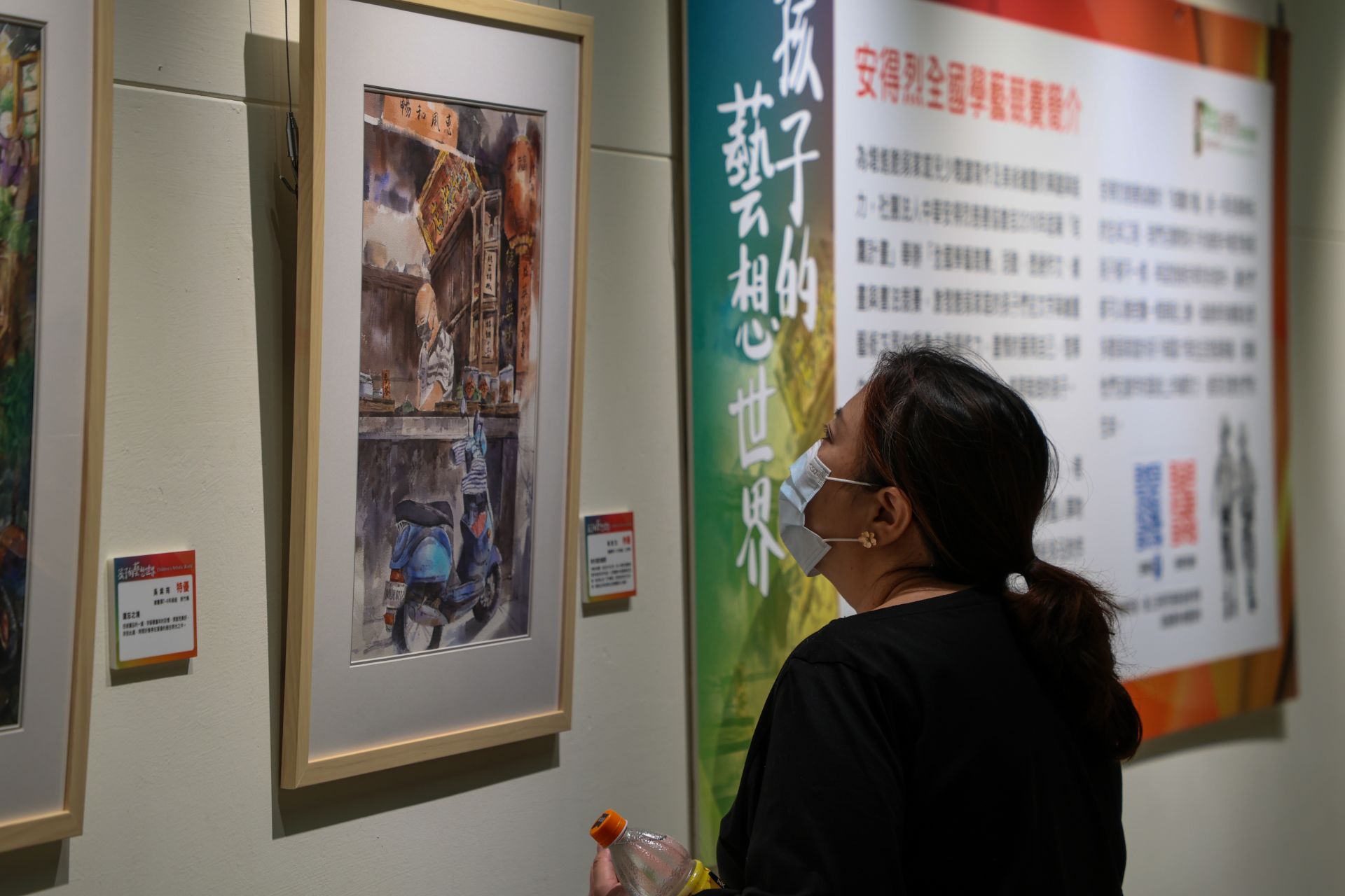 民眾近距離欣賞學生以水彩描繪的街巷風景作品，筆觸細膩且具生活感，展現弱勢兒少對城市日常的觀察與情感投射。（記者連琳攝）