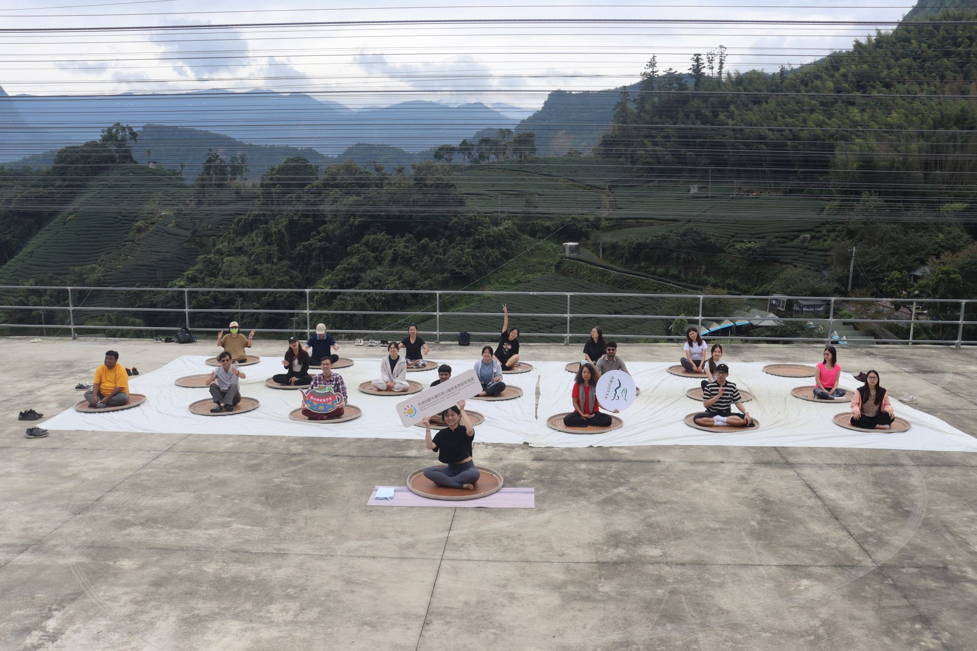 旅客在雲霧繚繞的茶園裡、隨著瑜珈老師伸展身心，旅人難得躺在竹編曬盤上呼吸清新空氣。（主辦單位提供） 