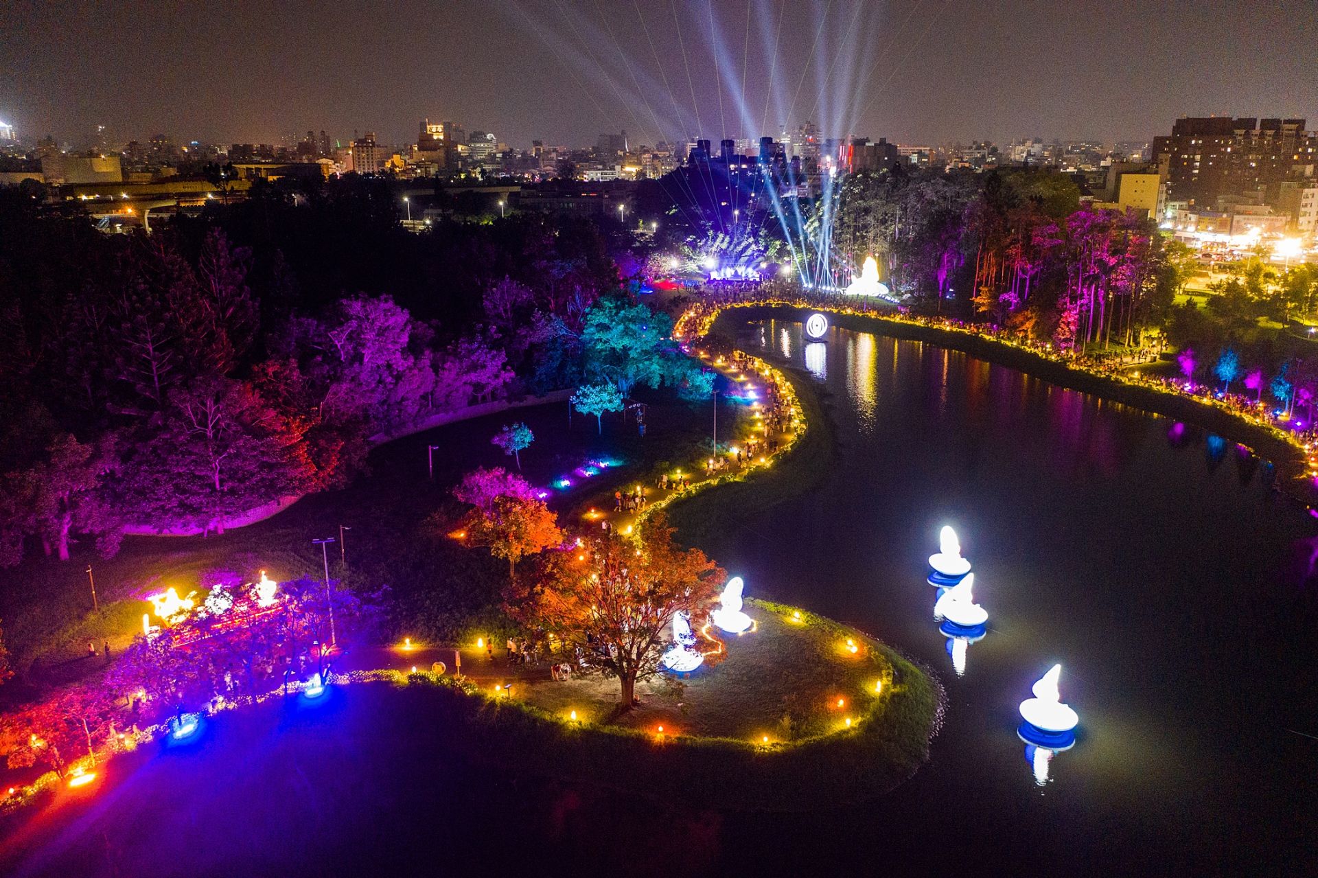 2025嘉義市光織影舞」展區中，9米高的愛麗絲主題裝置矗立花海間，湖畔的「光月疊影」旋轉月亮與水面倒影相互呼應景觀。(圖/嘉義市政府提供)