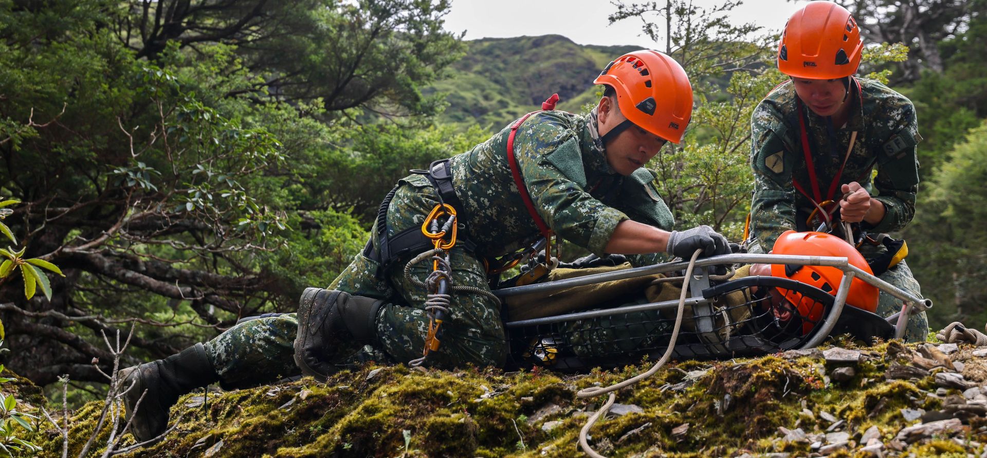 學員在碎石斜坡上方找到目標傷患，並實施繩索綑綁及擔架固定作業。（記者王子昌攝）