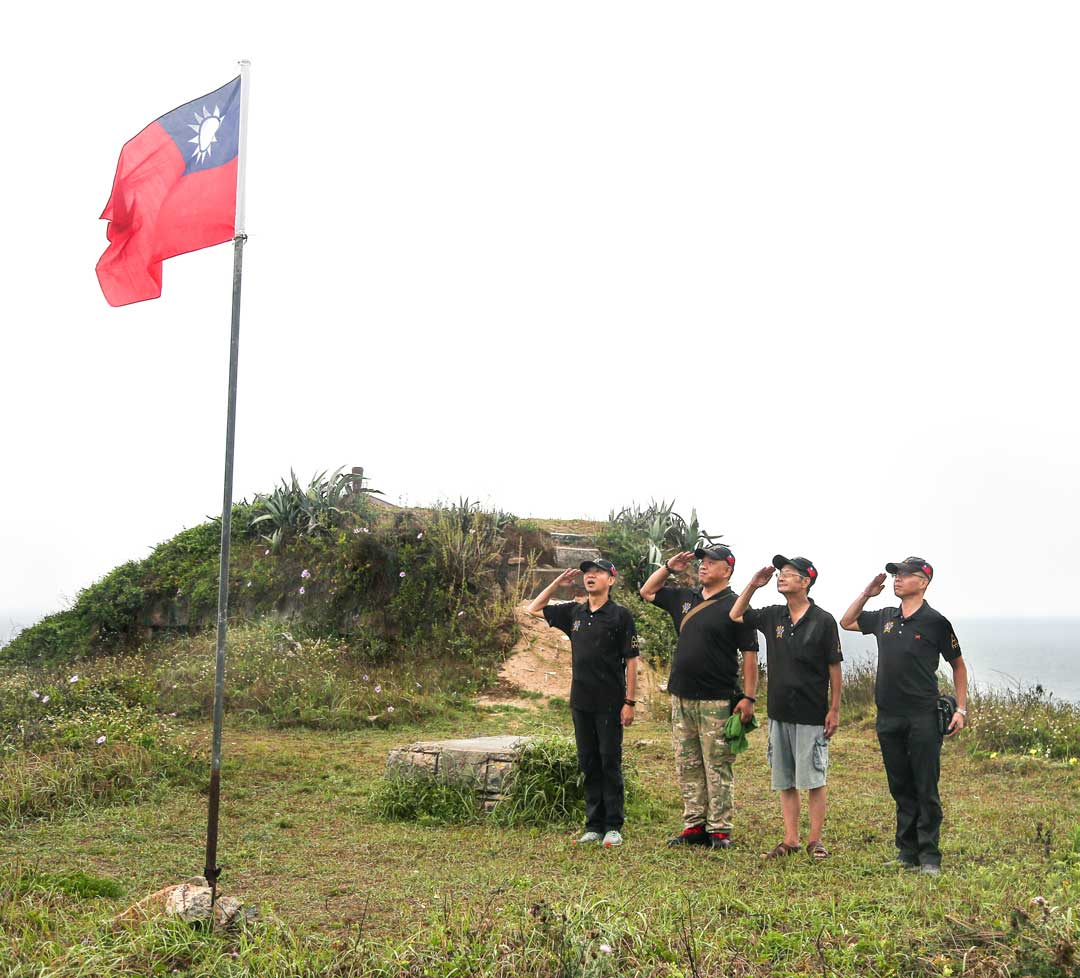鐘貫升(左二)與同袍以標準的敬禮姿勢，向飄揚的國旗行舉手禮。