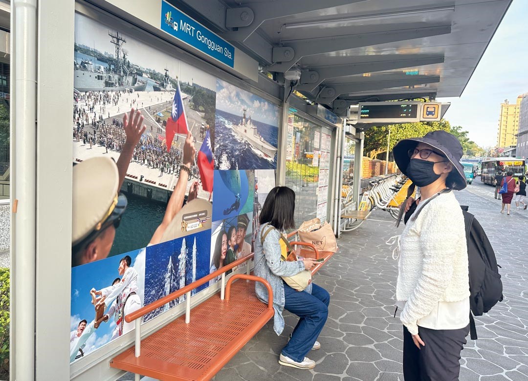 公車候車亭的民眾駐足凝視軍事攝影展，看見國軍官兵堅守崗位、保衛家園的精神。